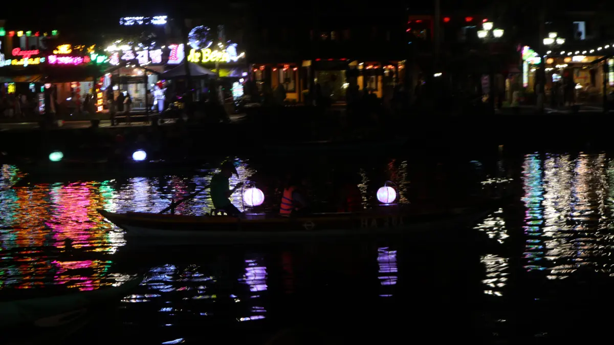 A boat on a river reflecting colorful night-market lights