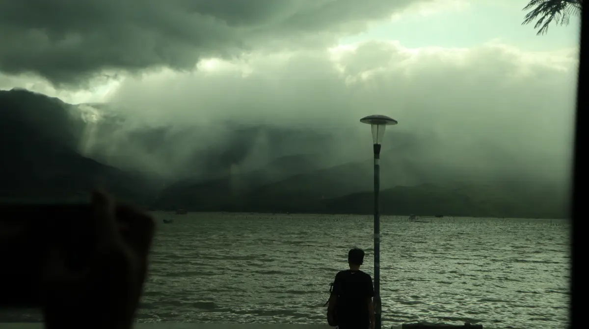 A person standing beside a mountain lake beneath storm clouds